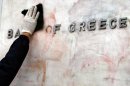 This Tuesday, Feb. 14, 2012 file photo, shows a worker cleaning a sign for the Bank of Greece from red and black paint, after Sunday's riots, in Athens. Austerity has been the main prescription across Europe for dealing with the continent's nearly 3-year-old debt crisis, brought on by too much government spending. Greece, one of three eurozone nations to need an international bailout, has cut spending on just about everything it can public sector salaries, pensions, education, health care and defense. (AP Photo/Thanassis Stavrakis)