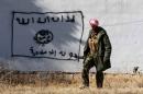 A Kurdish fighter walks by a wall bearing a drawing of the flag of the Islamic State group in the northern Iraqi town of Sinjar, in the Nineveh Province, on November 13, 2015