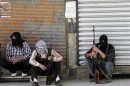 Free Syrian Army members, with covered faces and holding weapons, sit by the side of a street in Qaboun district, Damascus