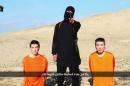 A masked person holding a knife speaks as he stands in between two kneeling men in this still image taken from an online video released by the militant Islamic State group