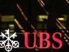 Employee uses a mobile phone as he walks past the logo of Swiss bank UBS in Zurich