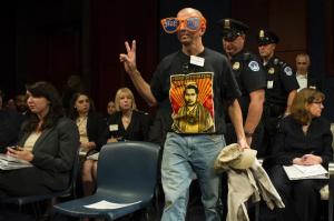 A protester is escorted out of the hearing as the Director …