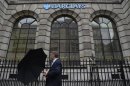 A man lifts his umbrella as he walks past a branch of Barclays bank in London
