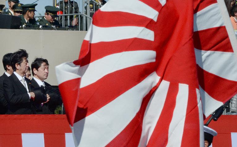 A Rising Sun flag flies in front of Japanese Prime Minister Shinzo Abe (L) as he inspects troops of Japan's Self-Defence Force during a military review at the Ground Self-Defence Force's Asaka training ground, on October 27, 2013