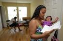 In this June 18, 2014 photo, Army Sgt. LaQuisha Gallmon, right, reads a letter from the Veterans Affairs Depart, as she holds her 2-month-old Abbagayle in Greenville, S.C. Gallmon said that her local VA office had authorized her to see a private physician during her pregnancy, so she went to an emergency room after experiencing complications in her sixth month of pregnancy. She said the VA has thus far refused to pay the resulting $700 bill. Gallmon's boyfriend Othneil Sands works on his laptop at left. (AP Photo/ Richard Shiro)
