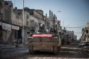 Turkish army vehicles drive in a street of the Syrian town of Kobane (aka Ain al-Arab) on February 22, 2015, during an operation to relieve the garrison guarding the Suleyman Shah mausoleum in northern Syria