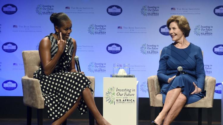 First lady Michelle Obama, left, points out her hairstyle as she sits with former first lady Laura Bush as they participate in the "Investing in Our Future" a discussion at the Kennedy Center in Washington, Wednesday, Aug. 6, 2014, as part of the US Africa Summit. Michelle Obama and Laura Bush, first ladies of different generations and opposing political parties, are uniting for the second time in just over a year to promote U.S. relations with Africa. (AP Photo/Susan Walsh)