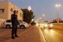 Riot police officer stands on the side of a highway as patrol vehicles are seen behind him during early hours of the evening in Manama