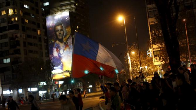 Fans wave a Chilean national flag as they walk past an advertising billboard with an image of Chile&#39;s striker Alexis Sanchez during celebrations after Chile&#39;s victory over Uruguay in their Copa America 2015 quarter-finals soccer match in Santiago