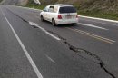 A car drives past a crack in a road after an earthquake on the outskirts of the town of Seddon in the Marlborough region
