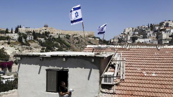 A man is seen from a window as Israeli flags fly on top of a house in Silwan neighborhood of east Jerusalem Thursday, Aug. 27, 2015. Ultra-nationalist Israelis have taken over the building in the heart of an Arab neighborhood in east Jerusalem, raising fears of fresh violence in the tense area. A small group of activists from the Ateret Cohanim settler organization moved into the building on Thursday. It was the latest in a wave of settler advances since nationalist Jews began buying up properties in Palestinian neighborhoods two decades ago. (AP Photo/Mahmoud Illean)