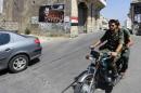 Two young Syrian soldiers ride a motorcycle past a huge poster bearing a portrait of President Bashar al-Assad next to a painting of a Syria's national flag in the Christian town of Marmarita in the central Homs region, on August 19, 2013