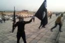 A fighter of the ISIL holds a flag and a weapon on a street in Mosul