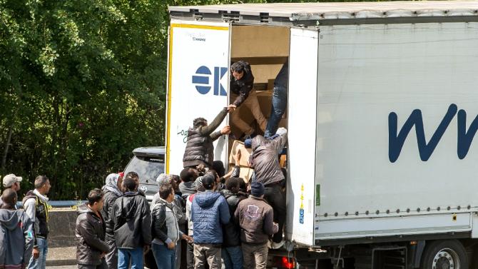 Migrants climb in the back of a lorry on the main highway leading to the Eurotunnel on June 23, 2015 in Calais, northern France