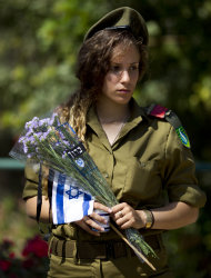 An Israeli soldiers prepares to place an Israeli flag with a black ribbon and flowers on the graves of fallen soldiers at the Kiryat Shaul Military Cemetery in Tel Aviv, Israel, Sunday, April 14, 2013. Israel will mark the annual Memorial Day in remembrance of soldiers who died in the nation's conflicts, beginning at dusk Sunday until Monday evening. Writing in Hebrew reads, "blessed." (AP Photo/Ariel Schalit)
