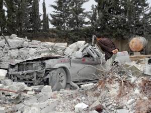 A Syrian man looks at the wreck of a car, buried under …