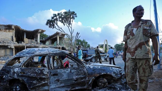 Soldiers and residents stand near wreckage of car and buildings after a bomb attack in Somalia&#39;s capital Mogadishu on February 27, 2016