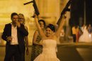 In this Sunday, Aug. 26, 2012 photo shot under iodine street lighting, a Romanian bride holds toy weapons in the air at the Triumph Arch in Bucharest, Romania. The arch, a replica of the Arc de Triomphe in Paris, the French capital, is a rendezvous place for brides on the wedding night for the bride stealing ritual. The ancient Romanian tradition of bride stealing is getting bigger, brasher and an increasingly common sight in the Romanian capital, the region's undisputed party town. (AP Photo/Vadim Ghirda)