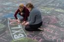 Two people write solidarity messages in chalk outside the stock exchange in Brussels on Tuesday, March 22, 2016. Explosions, at least one likely caused by a suicide bomber, rocked the Brussels airport and subway system Tuesday, prompting a lockdown of the Belgian capital and heightened security across Europe. At least 26 people were reported dead. (AP Photo/Geert Vanden Wijngaert)
