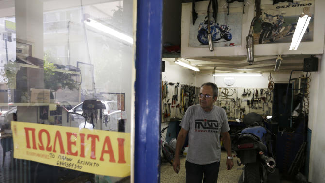 Mechanic Giorgos Prasinoudis steps out of his closed motorcycle repair shop, as a 'For Sale' sign is posted on the front window, in Athens, on Wednesday, July 22, 2015. Uncertainty over Greece's bailout and recent capital controls have led to a new spate of store closures in Greek capital. (AP Photo/Thanassis Stavrakis)