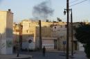 Smoke rises behind a Free Syrian Army fighter as he walks in Maysaloun neighborhood in Aleppo
