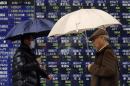 Pedestrians holding umbrellas walk past an electronic board showing stock prices outside a brokerage in Tokyo