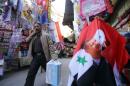A Syrian man walks past a Syrian flag bearing the portrait of Syrian President Bashar al-Assad in Hamidiya market in the Syrian capital, Damascus, on November 10, 2015