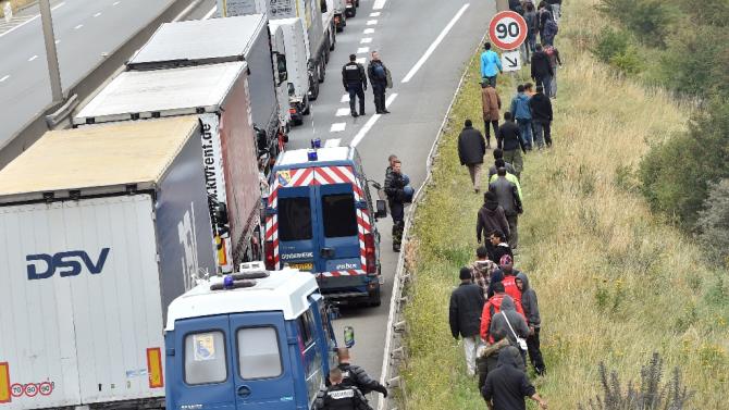 French police stand on the side of the road to prevent migrants from approaching lorries on the road leading to the ferry port in Calais, northern France, on August 5, 2015
