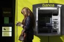 A woman stands beside an ATM at a branch of Spanish lender Bankia in Madrid
