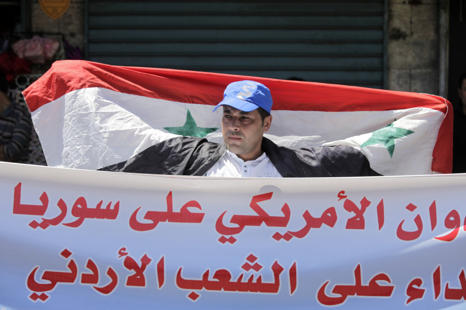 A Jordanian man holds the Syrian national flag during a protest by the Jordanian Communist Party and other leftist groups against any American military strike against Syria, in Amman, Jordan, Friday, Aug. 30, 2013. The Arabic banner reads "any American aggression on Syria it is considered as an American aggression on the Jordanian people." President Barack Obama prepared for the possibility of launching unilateral American military action against Syria within days as Britain opted out. Top U.S. officials spoke with certain lawmakers for more than 90 minutes in a teleconference Thursday evening to explain why they believe Syrian President Bashar Assad's government was the culprit in the suspected chemical attack last week. (AP Photo/Mohammad Hannon)