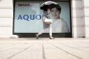A woman holding her umbrella walks past an advertisement poster for Sharp Corp's Aquos outside an electronics shop in Tokyo