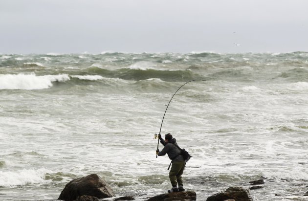 A fisherman stands on a rock to surf cast in the turbulent waves kicked up by Hurricane Sandy in Montauk, New York