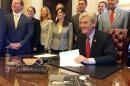 In this image provided by the Mississippi's Governor's Office, Mississippi Gov. Phil Bryant smiles as he signs the Protection Act, Friday, April 15, 2016, in Jackson, Miss. The law allows places of worship to designate some members to undergo firearms training and carry weapons inside church to protect the congregation. The governor's handgun rests on a book. (Clay Chandler/Mississippi's Governor's Office via AP)