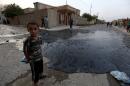 A boy stands near oil spill from wells in Qayyara