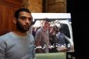 Syrian refugee Amjad Moghrabi stands in front of a photograph of his colleague, American aid worker Peter Kassig, 26, who converted to Islam while in captivity and changed his name to Abdul-Rahman Kassig, during an interview with The Associated Press in the northern port city of Tripoli, Lebanon, Saturday, Nov. 8, 2014. Kassig was helping victims of the Syrian civil war when he was captured in Syria last year and threatened with beheading by the Islamic State group. Arabic reads, "Justice for Abdul-Rahman." (AP Photo/Bilal Hussein)