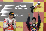 El alemán Sebastian Vettel, de la escudería Red Bull, lanza su trofeo al aire después de ganar el bicampeonato de la Fórmula Uno, en Suzuka, Japón, el domingo 9 de octubre de 2011. A su izquierda está el corredor británico Jenson Button, del equipo McLaren. (Foto AP/Greg Baker)