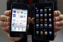 An employee of South Korean mobile carrier KT holds an Apple Inc's iPhone 4 smartphone and a Samsung Electronics' Galaxy S II smartphone as he poses for photographs at a registration desk at KT's headquarters in Seoul