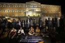Municipal public school guard Yiorgos Avramidis and other colleagues sit in front of a police line guarding the Greek parliament in Athens
