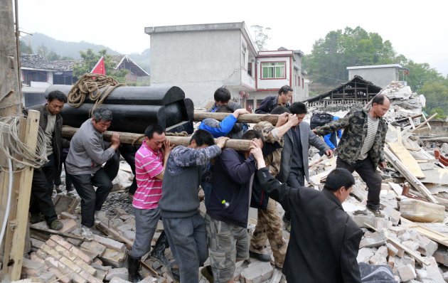 People lift a coffin as they walk past debris on their way to a funeral on the second day after an earthquake hit Longmen township of Lushan county