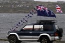 A "Yes" sign formed with cars is seen on a hill as a car decorated with Union Jack flags passes by in Stanley