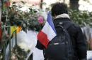 A man, carrying a French flag, passes by flowers, candles and messages left in tribute to victims near the Bataclan concert hall, one of the sites of deadly attacks, in Paris