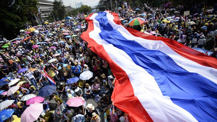 Anti-government protesters unveil a large Thai flag as they descend on Government House in Bangkok