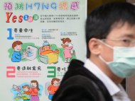 Homem se protege com máscara e cartaz dá orientações sobre a gripe
