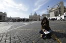 A media correspondent sits on the ground in Rome, as Saint Peter's Basilica at the Vatican is seen in the background