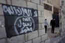 In this photo taken Oct. 28, 2014, two Jordanian men walk past graffiti depicting the flag of the Islamic State group with Arabic that reads, "There is only one God and Muhammad is his prophet," in the city of Ma'an, Jordan. Local authorities quickly stripped away public signs of support for the Islamic State group in this desert town. Black flags have been removed from rooftops. Graffiti proclaiming the extremists' imminent victory have been whitewashed. But supporters of the Middle East's most radical extremist group are only laying low. (AP Photo/Nasser Nasser)