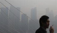 Indonesia desplegó el viernes aviones militares cisterna para combatir los incendios forestales que han causado unos niveles récord de una peligrosa niebla en la vecina Singapur por tercer día consecutivo, en una de las peores crisis de contaminación aérea del sureste de Asia. En la imagen, un hombre fuma un cigarrillo con el skyline de Singapur, cubierto por la niebla, de fondo, el 19 de junio de 2013. REUTERS/Edgar Su