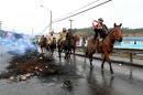 Local residents riding horses pass along a burnt out barricade in a street of Castro, Chiloe island on May 9, 2016