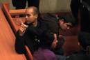 Juan Flores, left, waves to an unidentified person in the back of the courtroom as he sits handcuffed alongside fellow suspects Guillermo Duran, top right, and Nataly Casanova during their hearing in Santiago, Chile, Tuesday, Sept. 23, 2014. The three are alleged members of an anarchist cell suspected in a Sept. 8 bomb attack that injured 14 people. The judge ordered they remain in jail, or under house arrest, and gave prosecutors 10 months to gather evidence against the suspects under Chile's anti-terrorism law. (AP Photo/Luis Hidalgo)