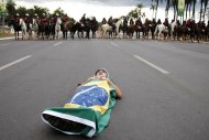 Manifestante se deita no chão, enrolado com a bandeira do Brasil, em frente a policiais montados perto do estádio Mané Garrincha, em Brasília