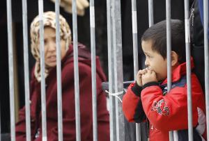 Young boy looks through bars as group of migrants waits&nbsp;&hellip;